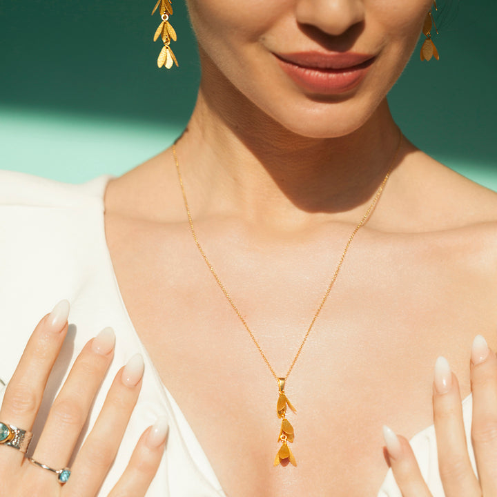 Woman wearing a gold catkin flower necklace and earrings with a green background