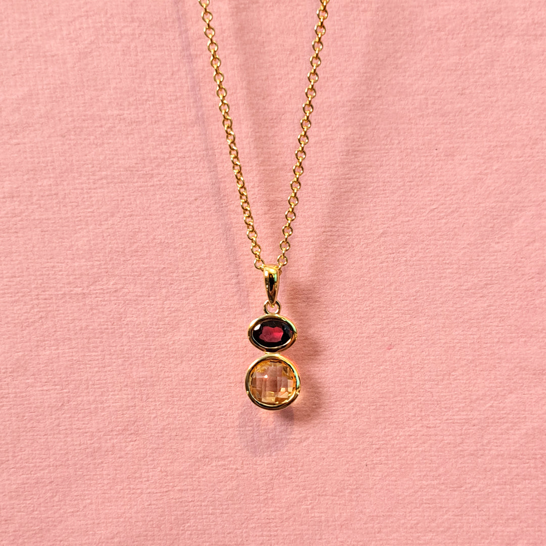 Gold necklace with citrine and garnet gemstones on a pink background