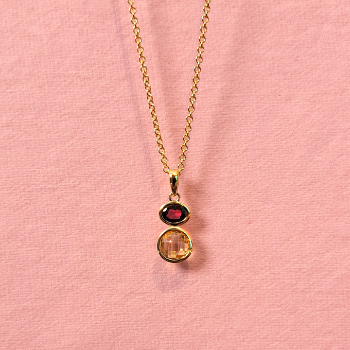 Gold necklace with citrine and garnet gemstones on a pink background