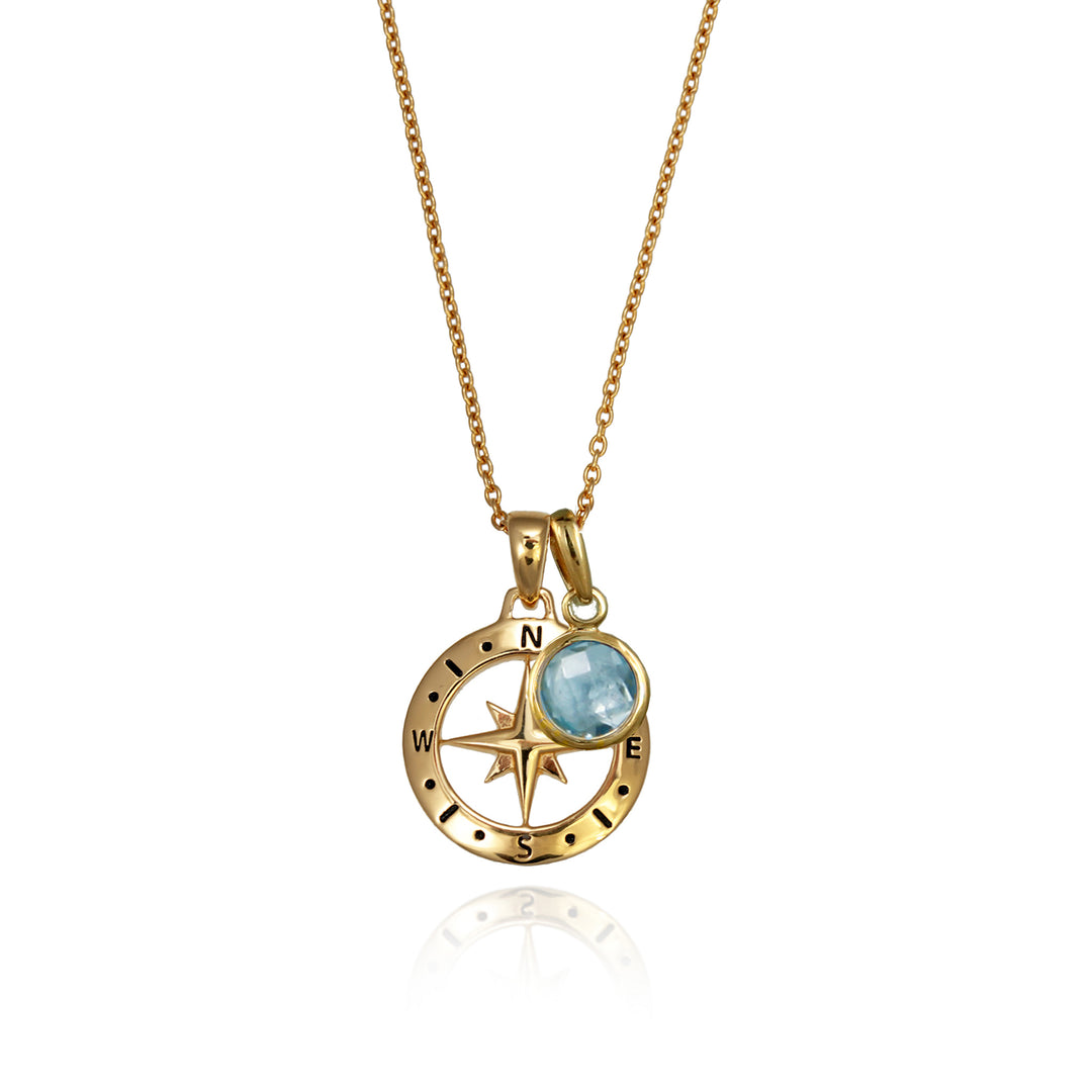 A gold versible compass necklace with a blue topaz december birthstone charm and chain against a white background