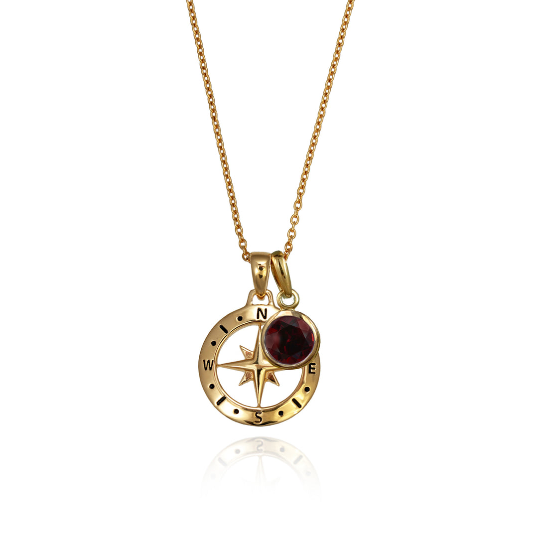 A gold versible compass necklace with a red garnet january birthstone charm and chain against a white background