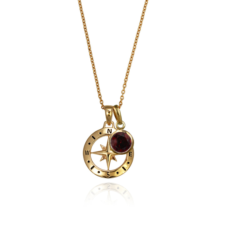 A gold versible compass necklace with a red garnet january birthstone charm and chain against a white background