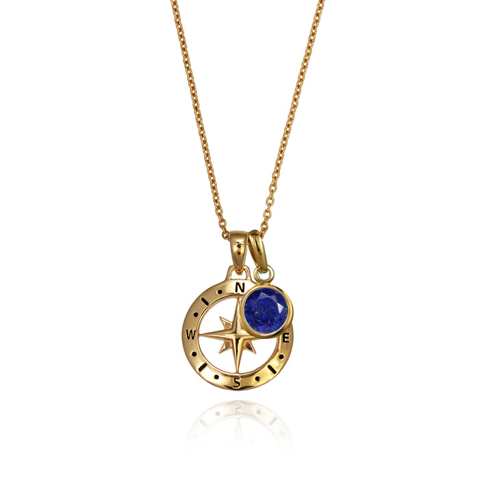 A gold versible compass necklace with a deep blue lapis september  birthstone charm and chain against a white background