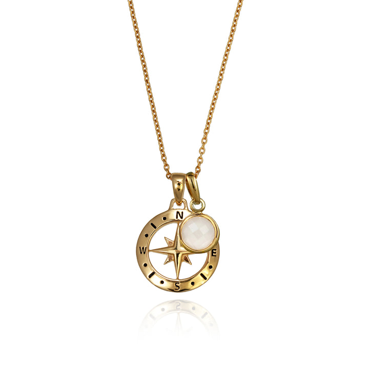 A gold versible compass necklace with a moonstone june birthstone charm and chain against a white background