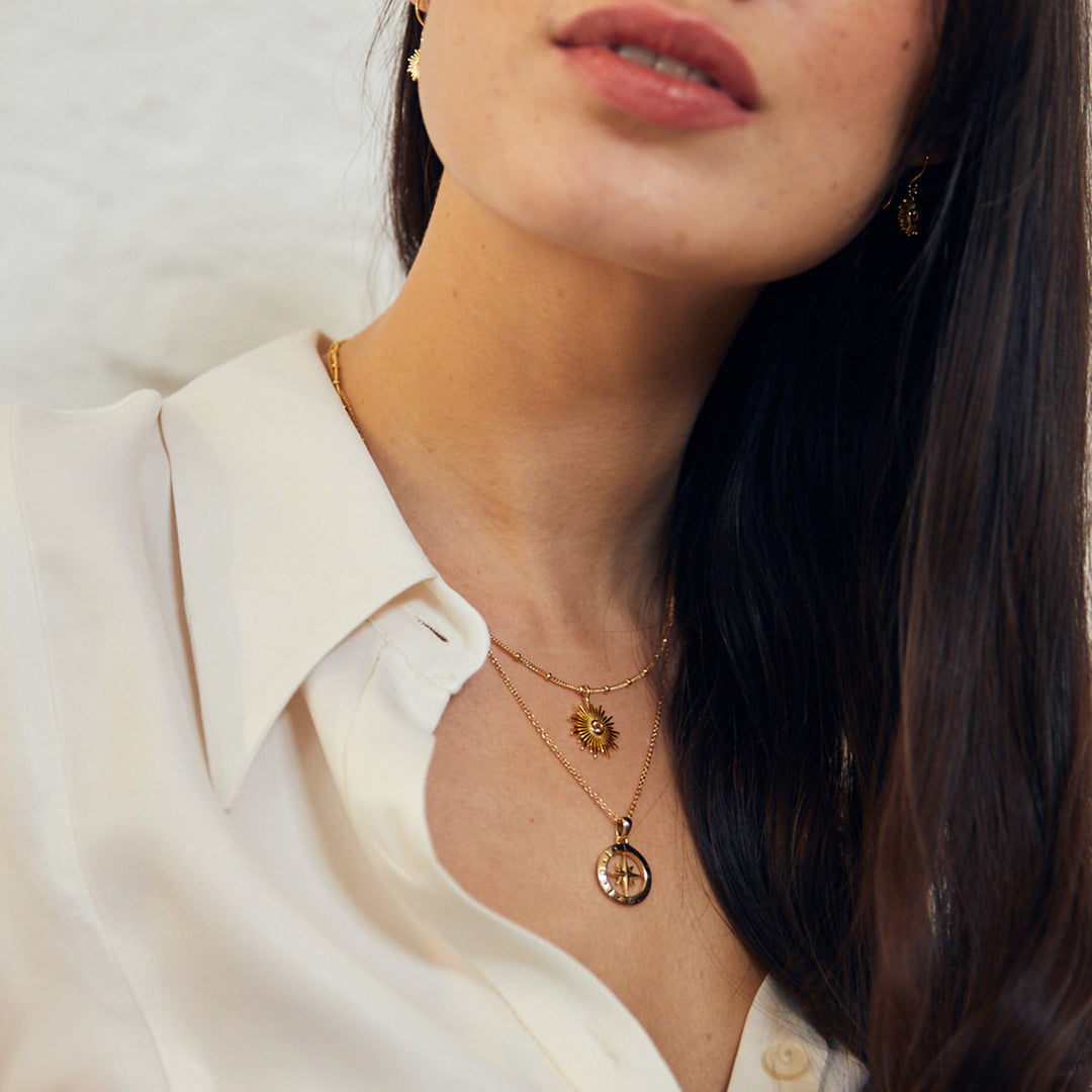 Model wearing gold compass and sun pendants