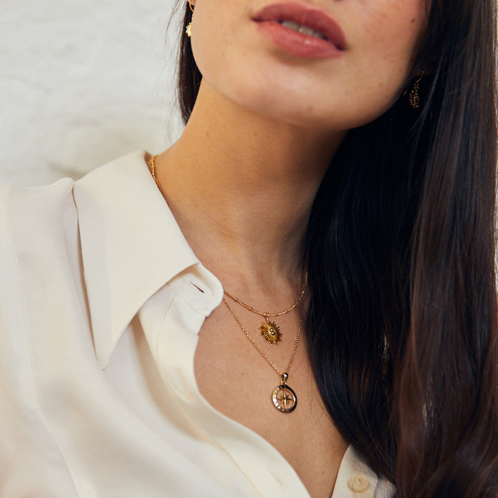 Model wearing gold compass and sun pendants