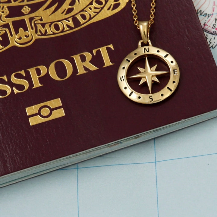 18ct  gold vermeil compass pendant necklace on top of a passport