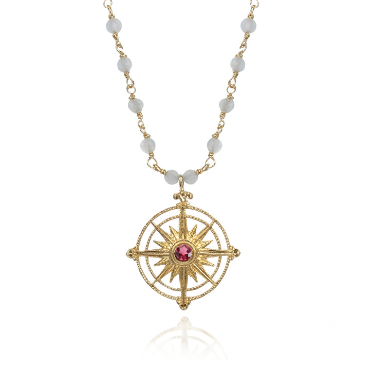 Gold compass pendant with a pin tourmaline gemstone on a blue chalcedony chain on a white background.