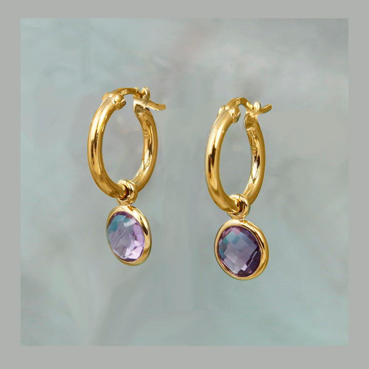 Gold hoop earrings with purple gemstones on a light gray background