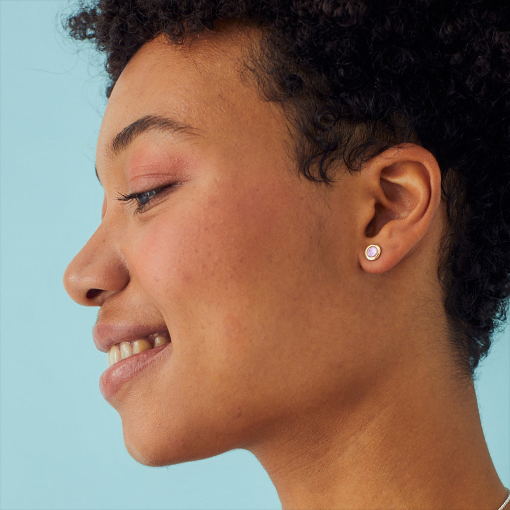 Close-up of model wearing gold stud earrings with pink gemstones.