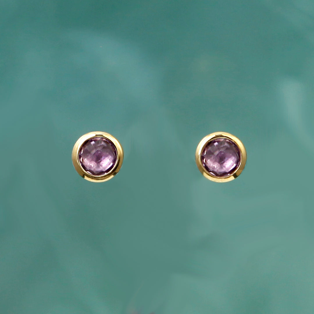 Round gold post earrings with purple gemstones on an aqua background