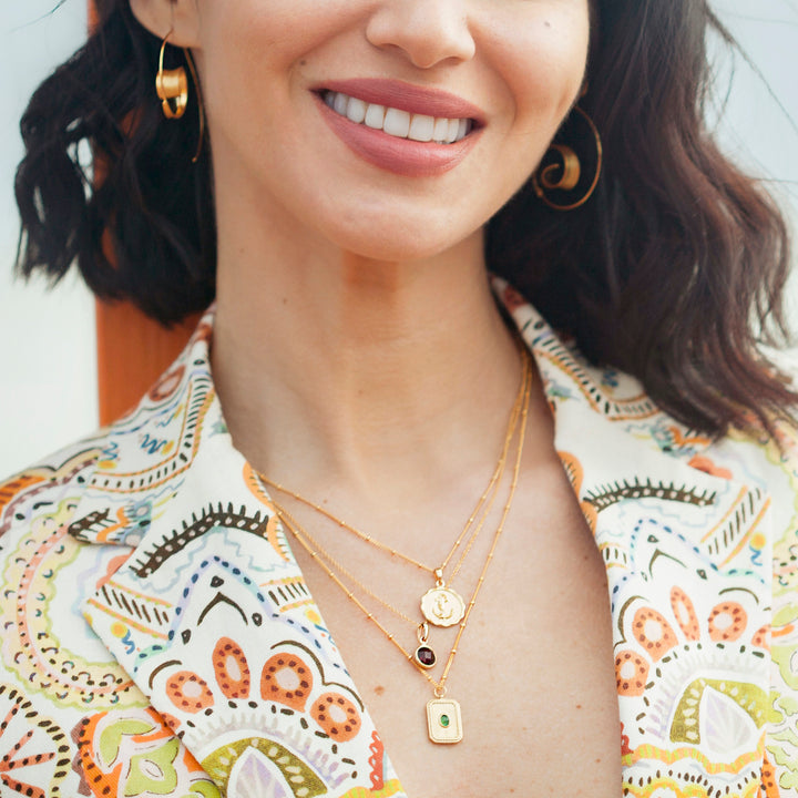 Woman wearing several gold necklaces including ruby birthstone pendant