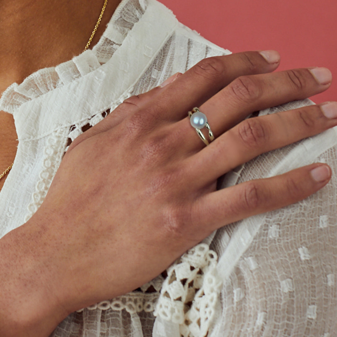 Model wearing a gold and pearl ring with pink background