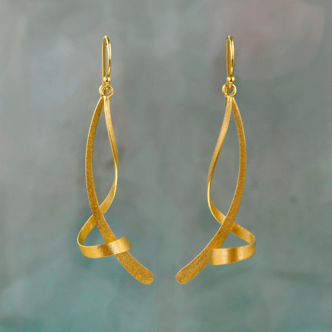 Gold twisted dangle earrings on a gray background