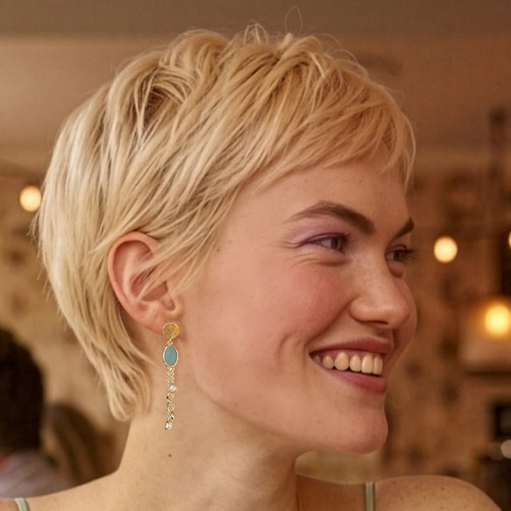 Model wearing gold chalceony stud earrings with blue topaz and pearl and chain drops.