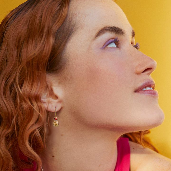 Close-up of a woman wearing gold earrings set with citrine and garnet gemstones