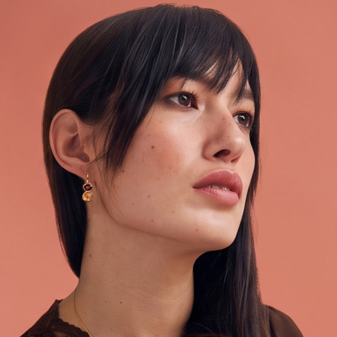 Woman wearing 18ct gold vermeil citrine and garnet drop earrings against a sienna coloured background