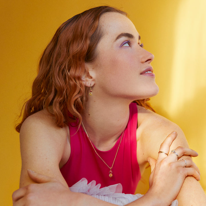Woman in a pink top wearing matching gold earring and necklace set featuring citrine and garnet gemstones