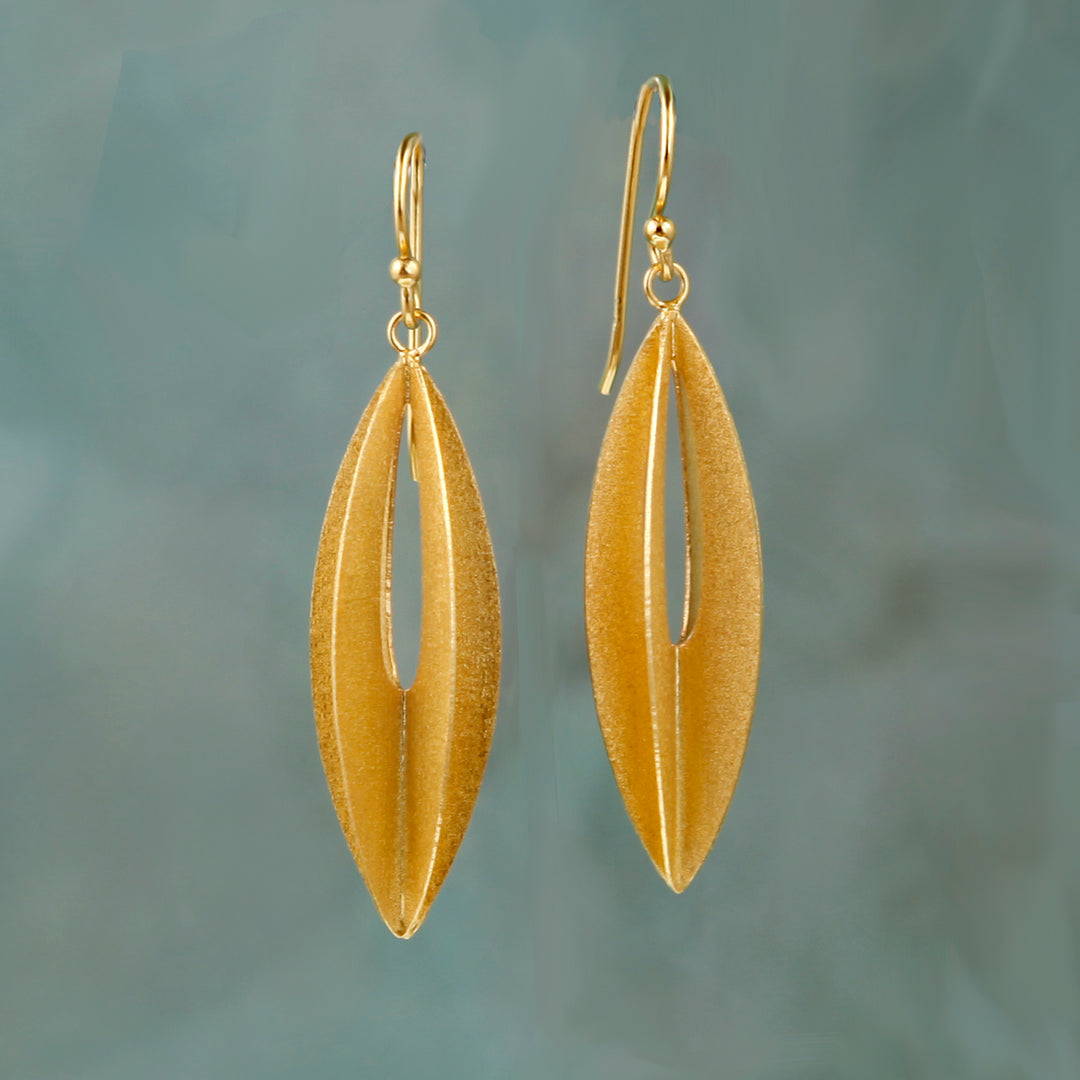 Gold geometric elliptic shaped earrings against an aqua background