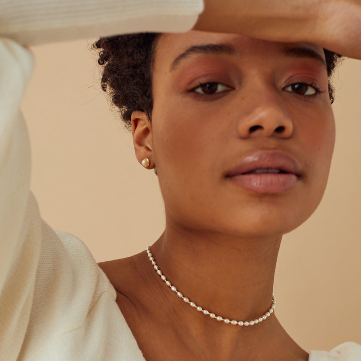 Woman wearing a pearl necklace and matching stud earrings against a beige background