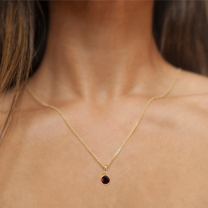 Model wearing a gold garnet pendant on a gold chain