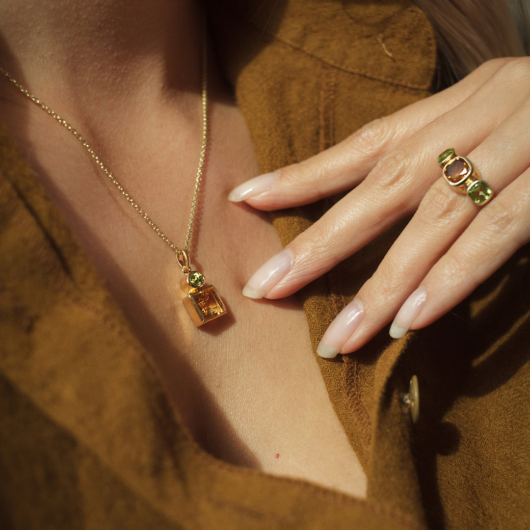 Close-up of a model wearing a gold ring with matching necklace with citrine and garnet