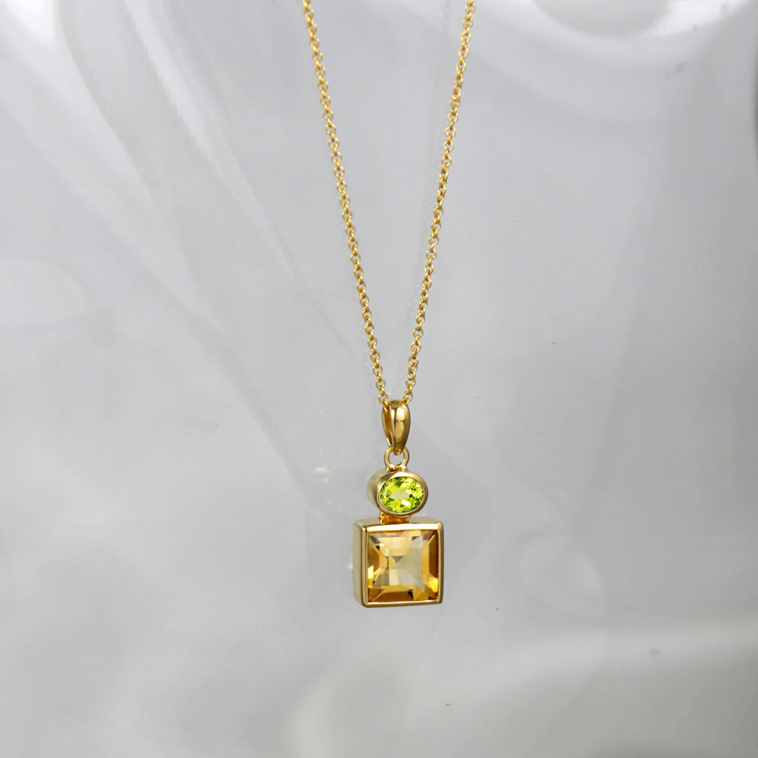 Gold necklace with a pendant featuring a square-cut yellow citrine gemstone and oval peridot on a white background