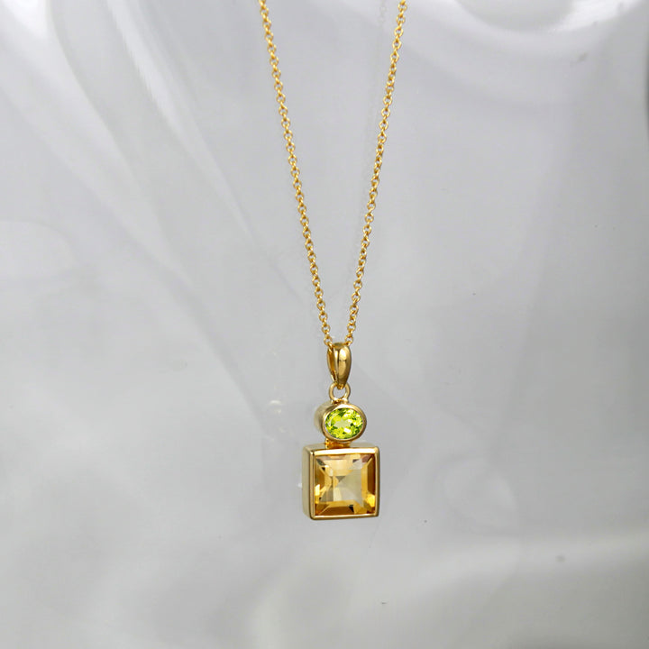 Gold necklace with a pendant featuring a square-cut yellow citrine gemstone and oval peridot on a white background