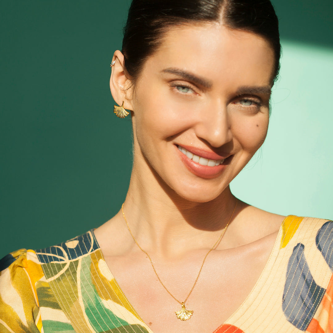Woman wearing gold ginkgo earrings and matching necklace with a printed top