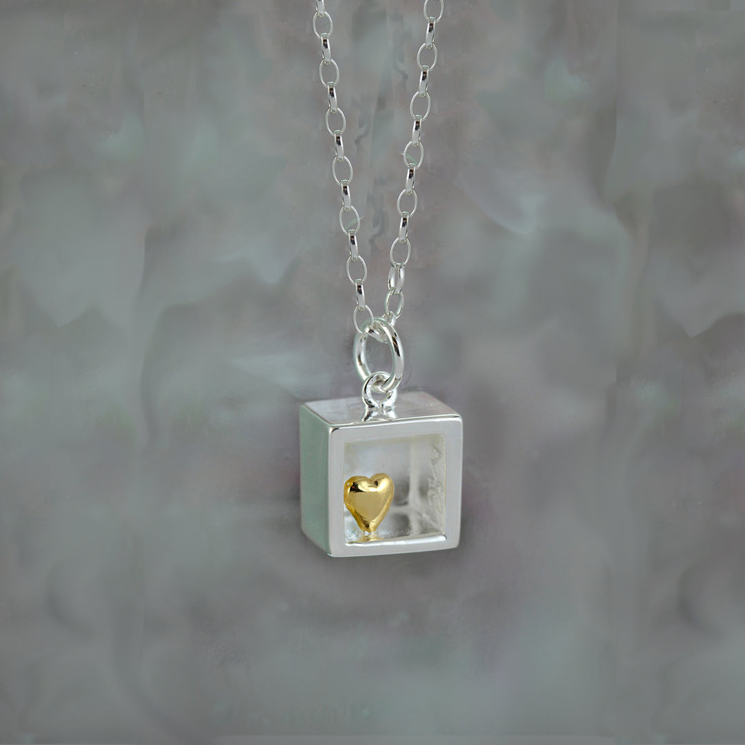 Necklace with a square pendant containing a gold heart charm on a gray background