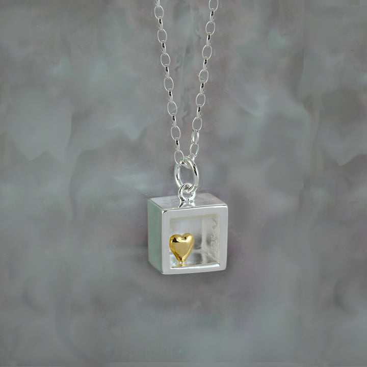 Necklace with a square pendant containing a gold heart charm on a gray background