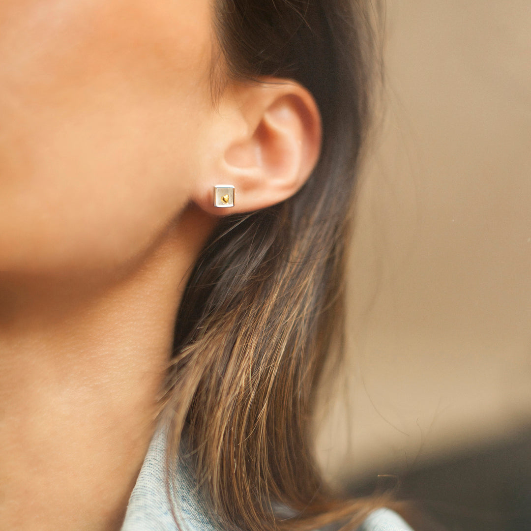 Close-up model wearing a small silver earring with a gold heart inside
