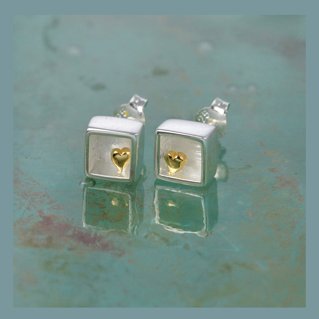 Silver square earrings with gold heart inside on a textured green surface