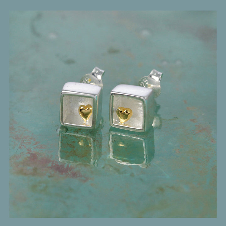 Silver square earrings with gold heart inside on a textured green surface