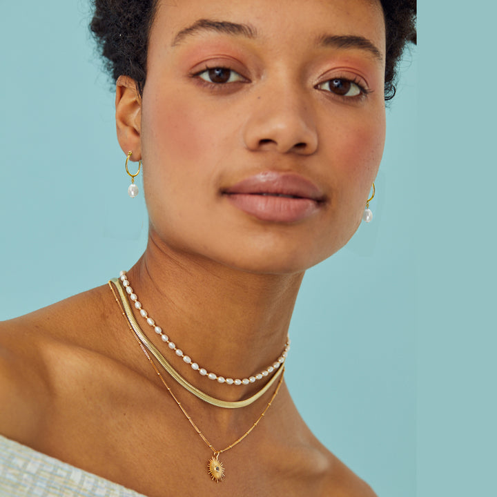 Model wearing gold necklaces with string of pearls and matching hoop earrings