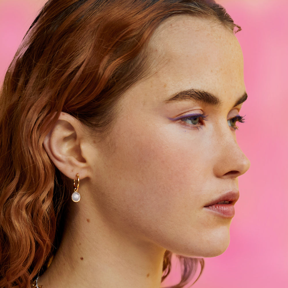 Model wearing gold snap-post hoop earrings with pale rose quartz gemstones.