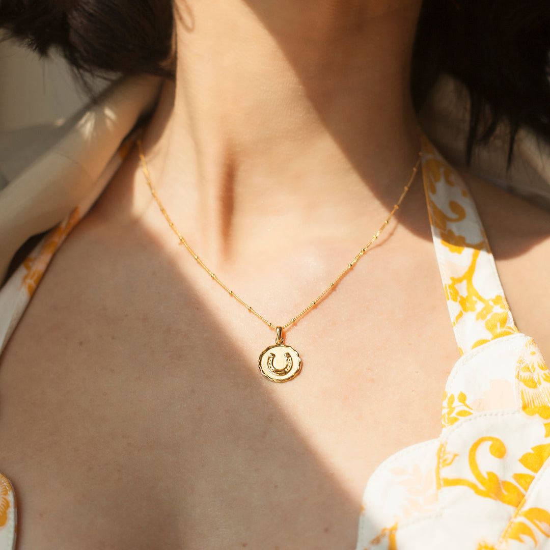 Model wearing a gold horseshoe necklace and a printed dress
