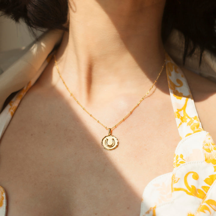 Model wearing a gold horseshoe necklace and a printed dress