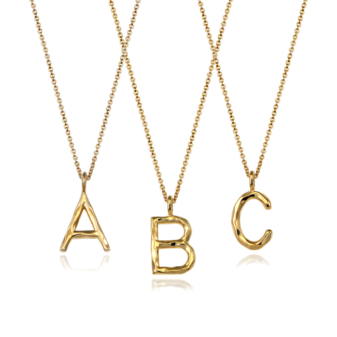 Three gold initial letter pendants with chains on a white background