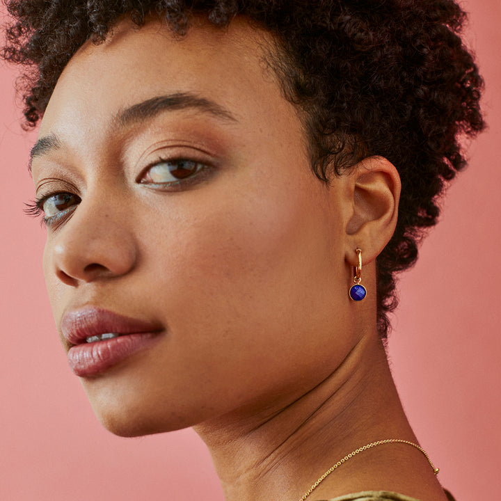 Side view of model wearing gold hoop earrings with blue gemstones
