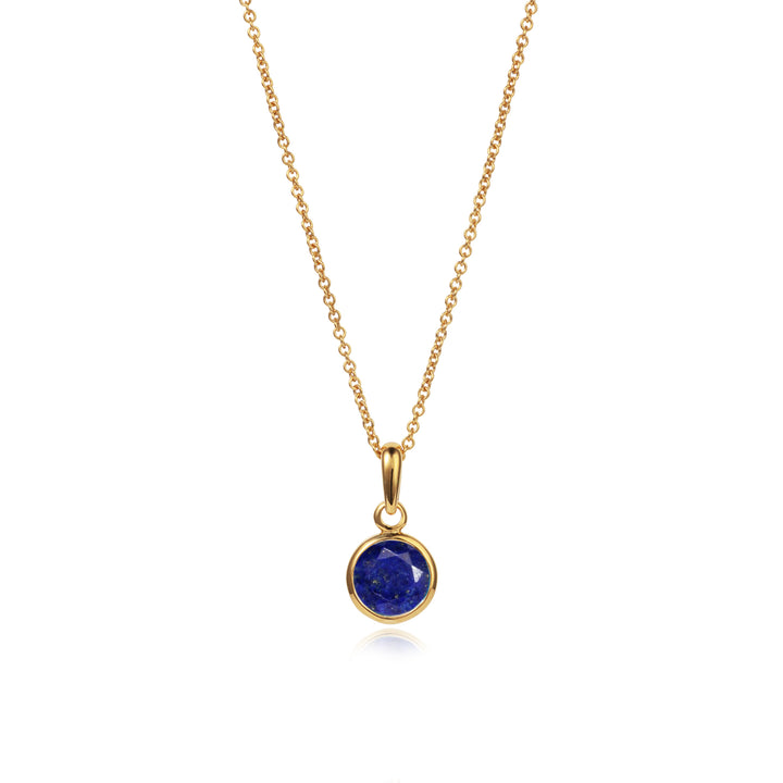 Dainty gold necklace with a round blue lapis lazuli stone and chain on white background