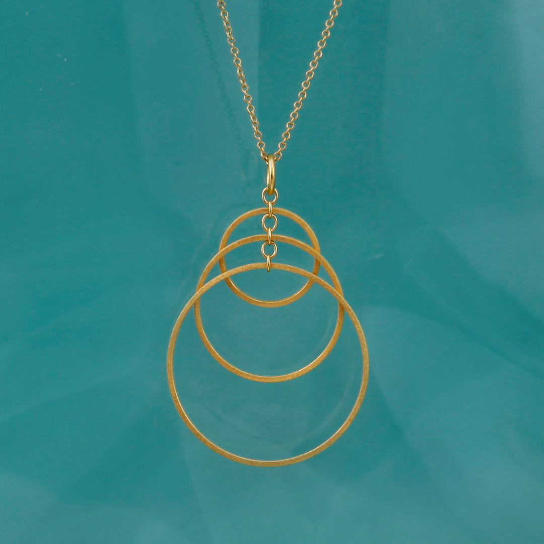 Gold necklace with three interlocking rings on a teal background