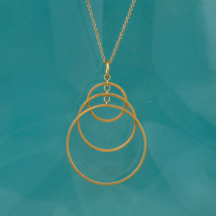 Gold necklace with three interlocking rings on a teal background