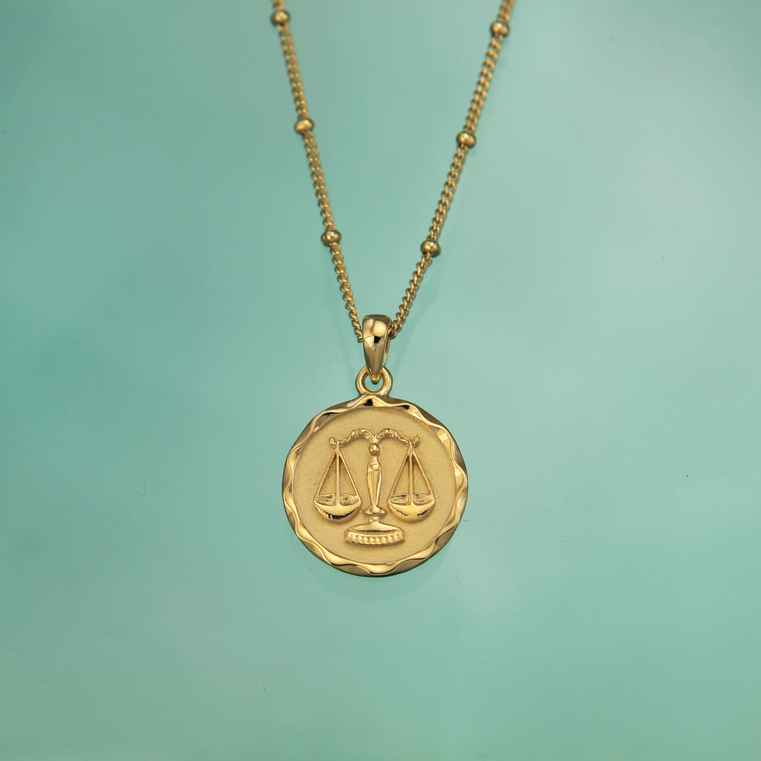 Gold Libra zodiac star sign necklace pendant on an aqua background
