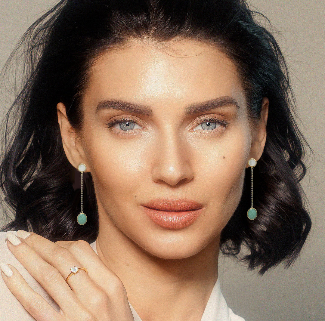 Model wearing long chain earrings with a white and green gemstone