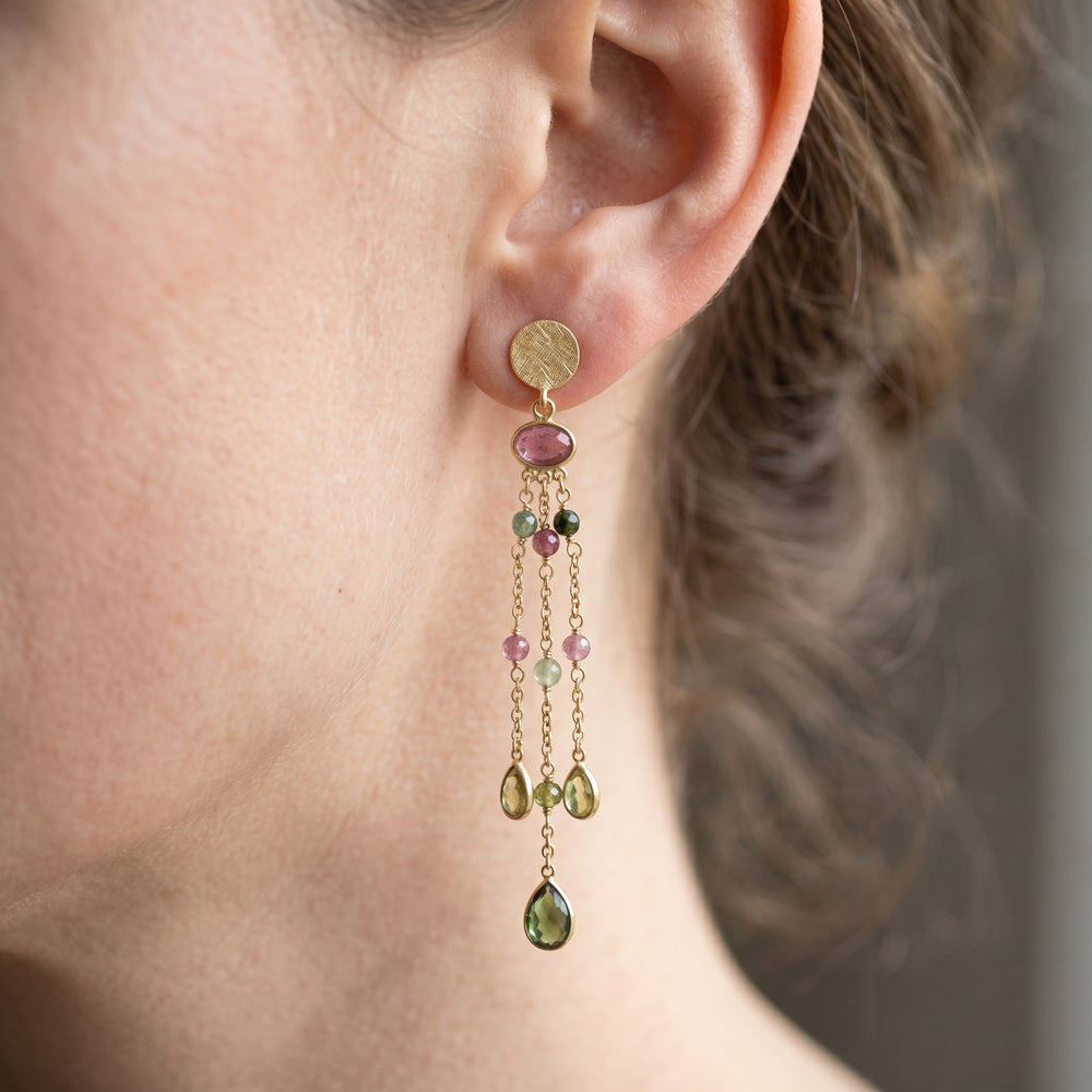 Close-up of model wearing long gold crop earrings featuring multi-coloured tourmaline gemstones on fine chain drops.