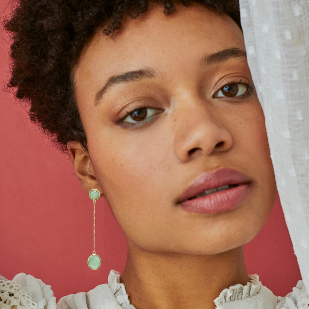 Model wearing long dangle gold earrings with two green aventurine stones
