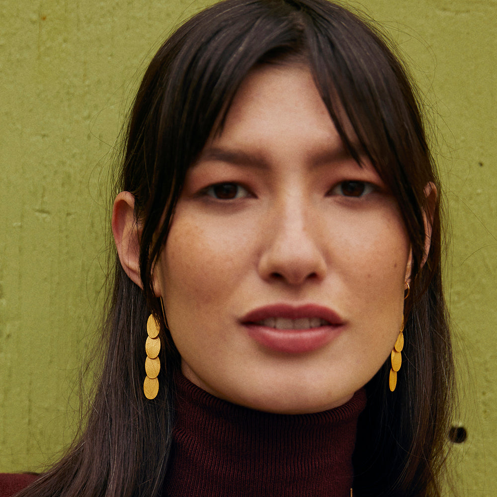 model wearing gold, oval disk chandelier earrings.