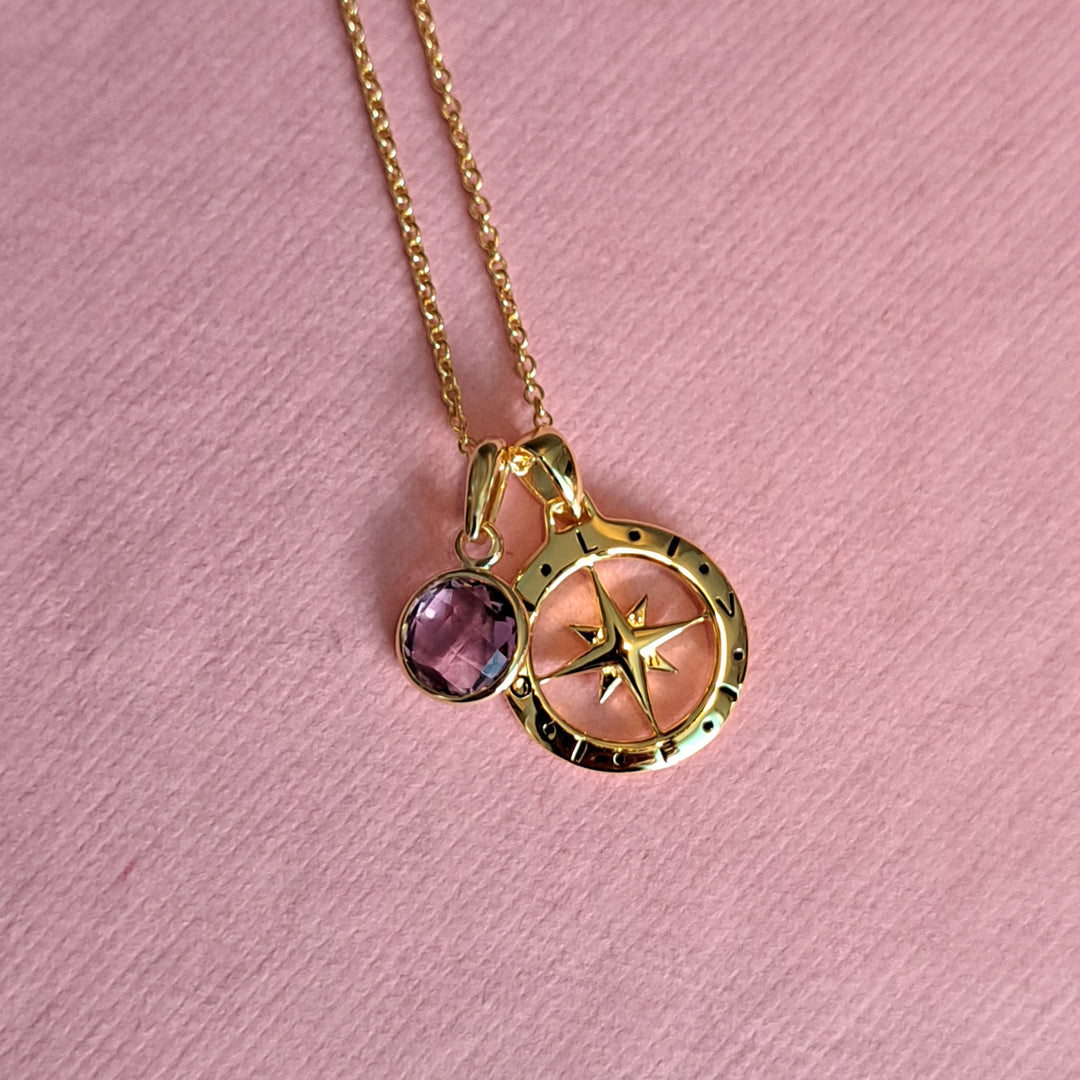 Close-up of gold compass necklace with an amethyst birthstone charm