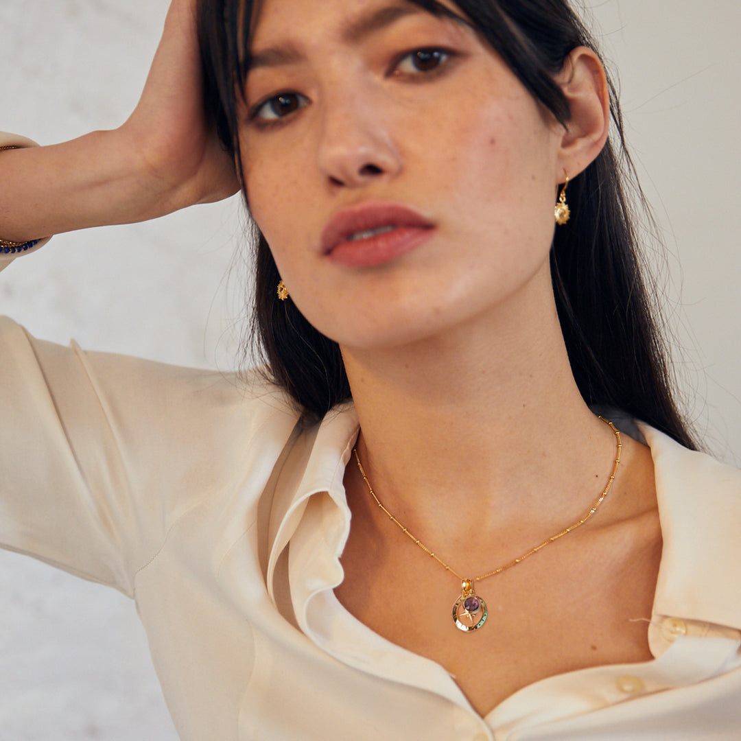 Model wearing a gold compass necklace with amethyst february birthstone charm
